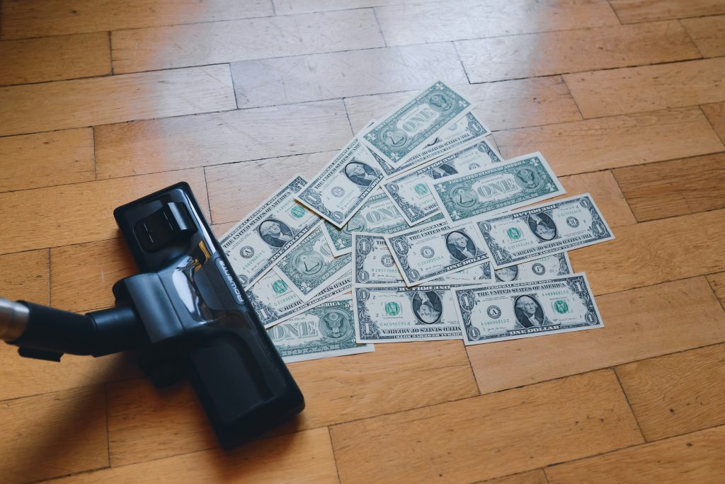 Vacuum cleaner sucking up dollar bills on a wooden floor.