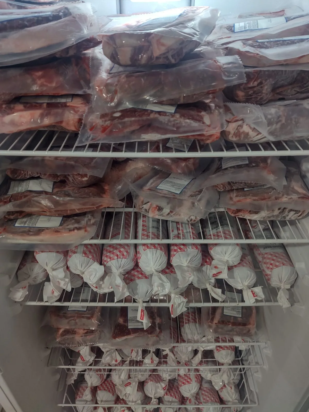 Close-up of freezer shelves packed with vacuum-sealed beef and red-and-white checkered paper-wrapped packages