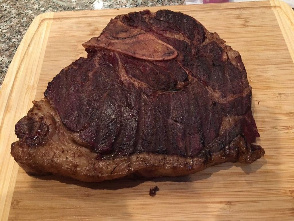 A large grain-finished T-bone steak from Nadig Farms resting on a wooden cutting board.