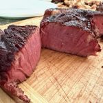 Sliced grain-finished steak showing a rare pink center and seared crust, fanned out on a wooden cutting board — Nadig Farms Angus beef.