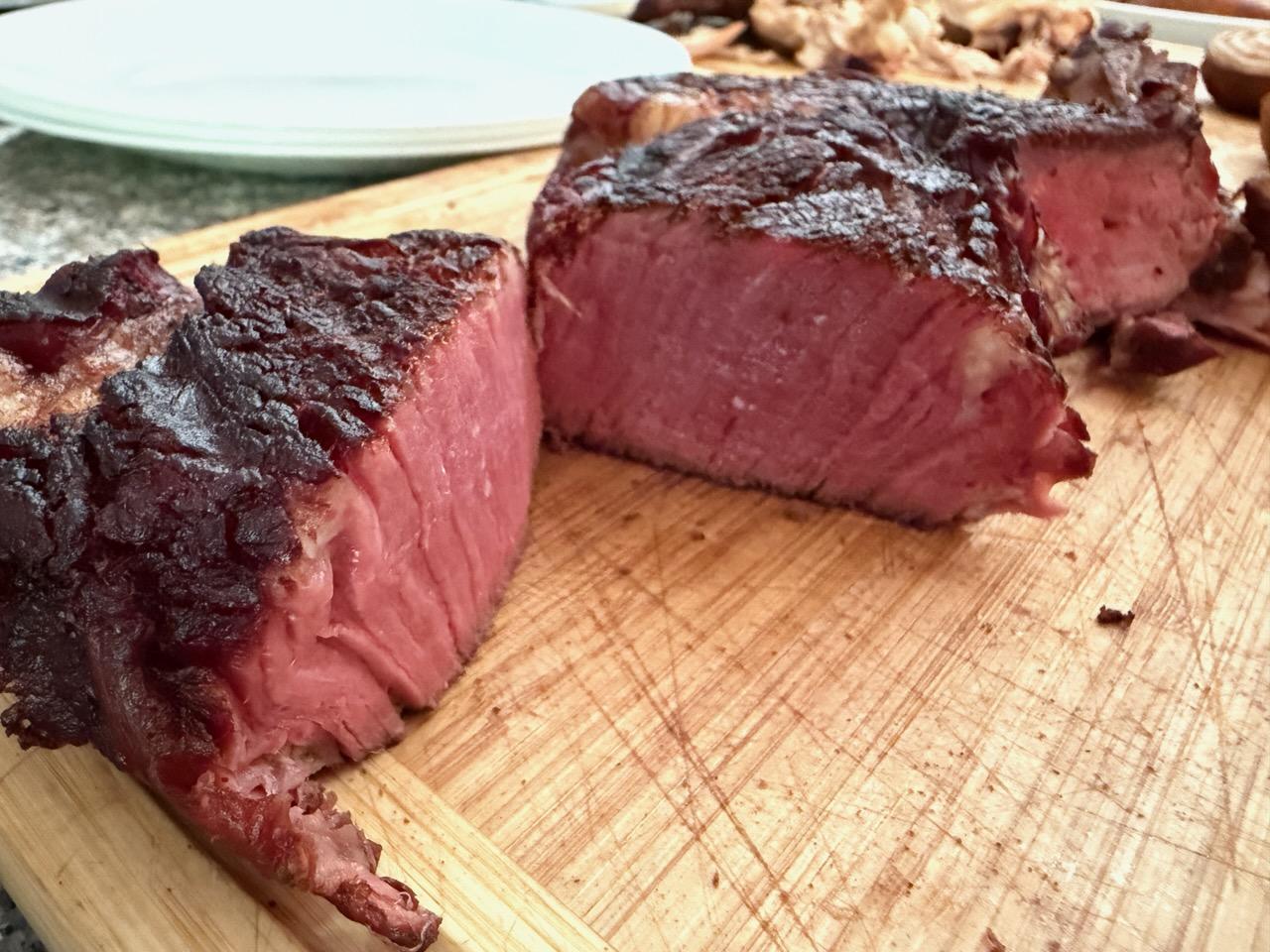 Sliced grain-finished steak showing a rare pink center and seared crust, fanned out on a wooden cutting board — Nadig Farms Angus beef.